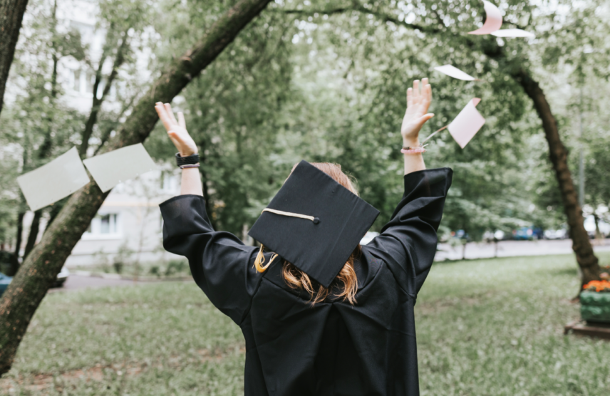 Graduate in cap and gown celebrating on a campus lawn